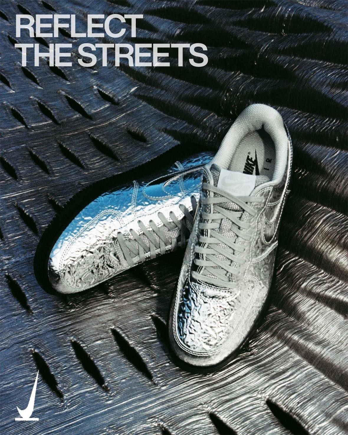 Par de Nike Air Force 1 '01 Chrome con el upper plateado arrugado y reflectivo y la suela negra, apoyado sobre una superficie oscura texturada, en la imagen oficial de SNKRS con la frase Reflect the Streets