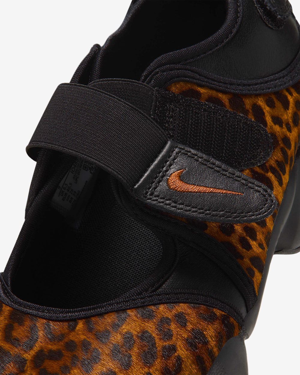 Primer plano del strap negro del Nike Air Rift Black/Desert Ochre, con la lengüeta de cuero y el Swoosh bordado en ocre, sobre el pelo ocre con manchas negras y la abertura negra del calzado