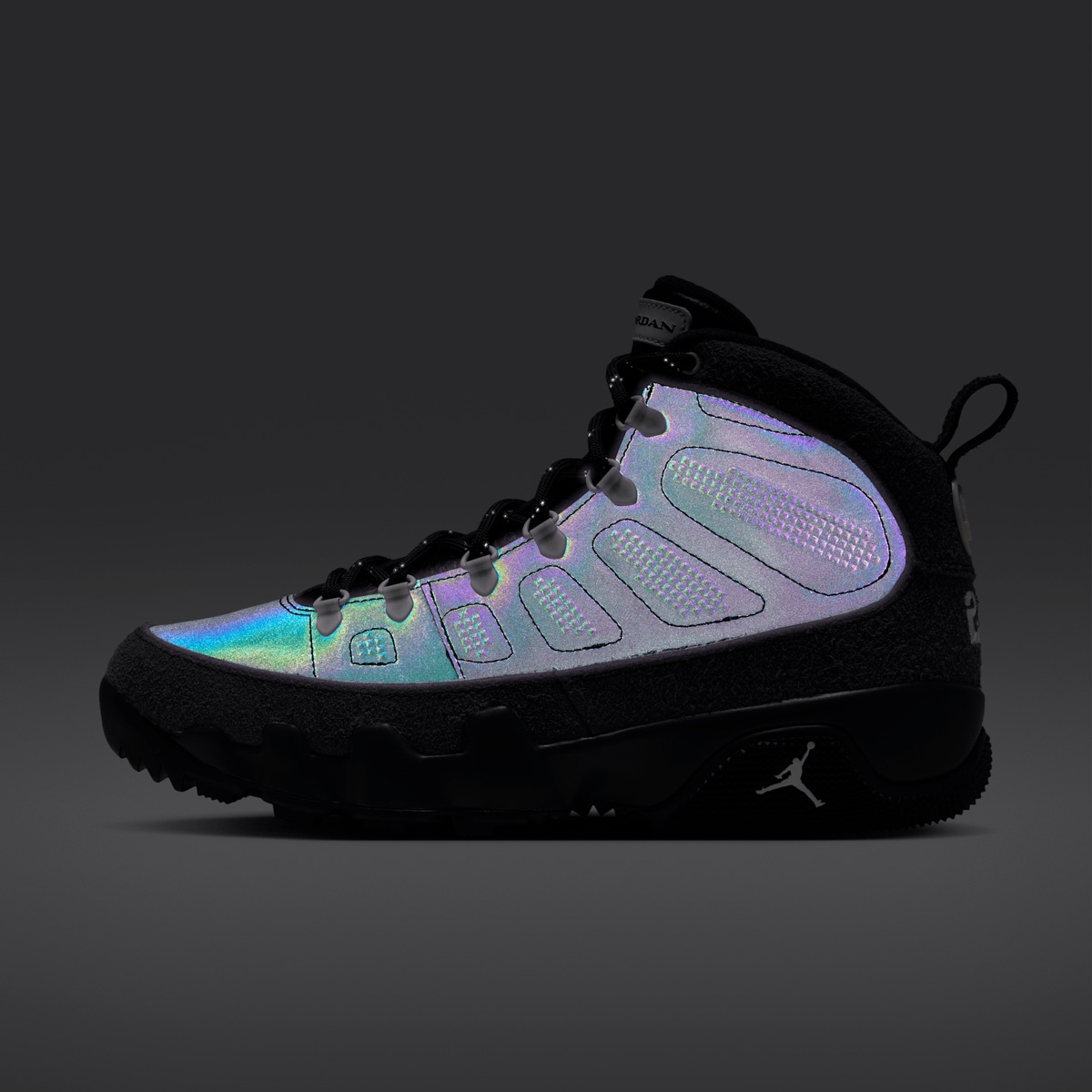 Air Jordan 9 Retro Boot NRG Anthracite de perfil sobre fondo gris oscuro, con los paneles laterales reflectivos brillando en tonos lila, celeste y verde, gamuza gris oscura en la base y el talón y suela negra con el Jumpman blanco