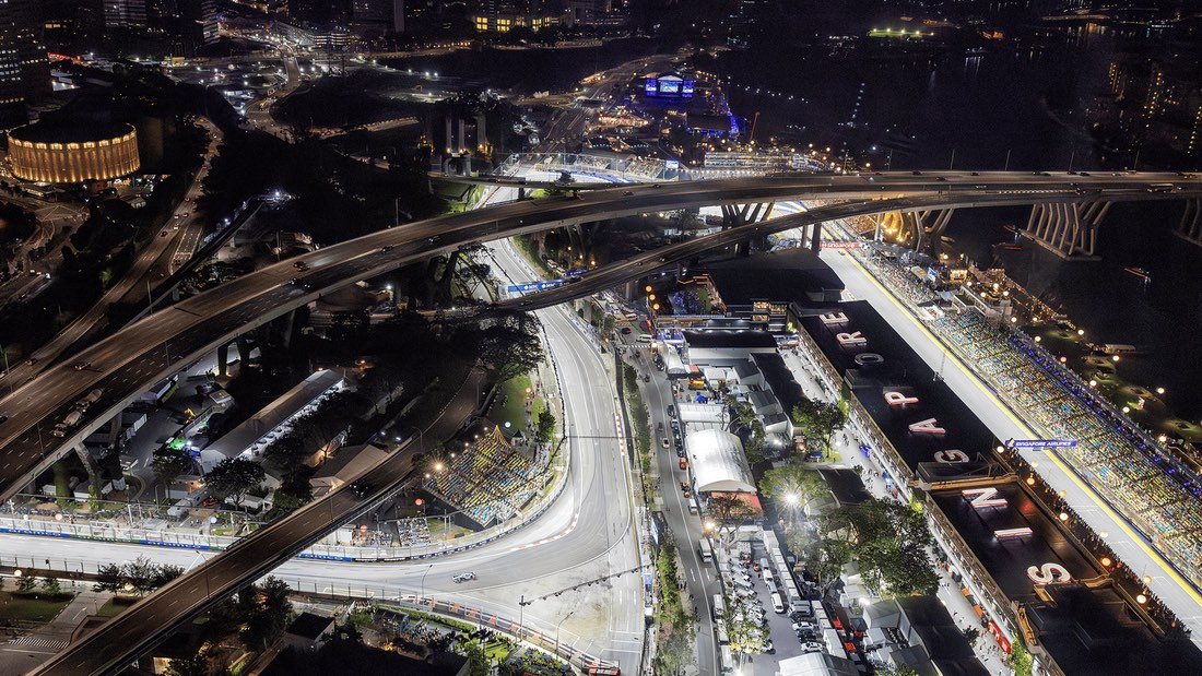 Vista aérea nocturna del circuito callejero de Marina Bay, con la recta de boxes iluminada, las tribunas llenas y las autopistas que pasan por encima del trazado