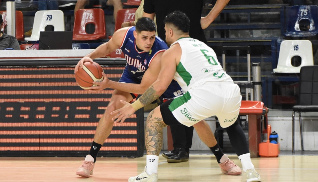 Un jugador de Quimsa con la camiseta azul protege la pelota ante la marca de un jugador de Atenas con la camiseta blanca 6