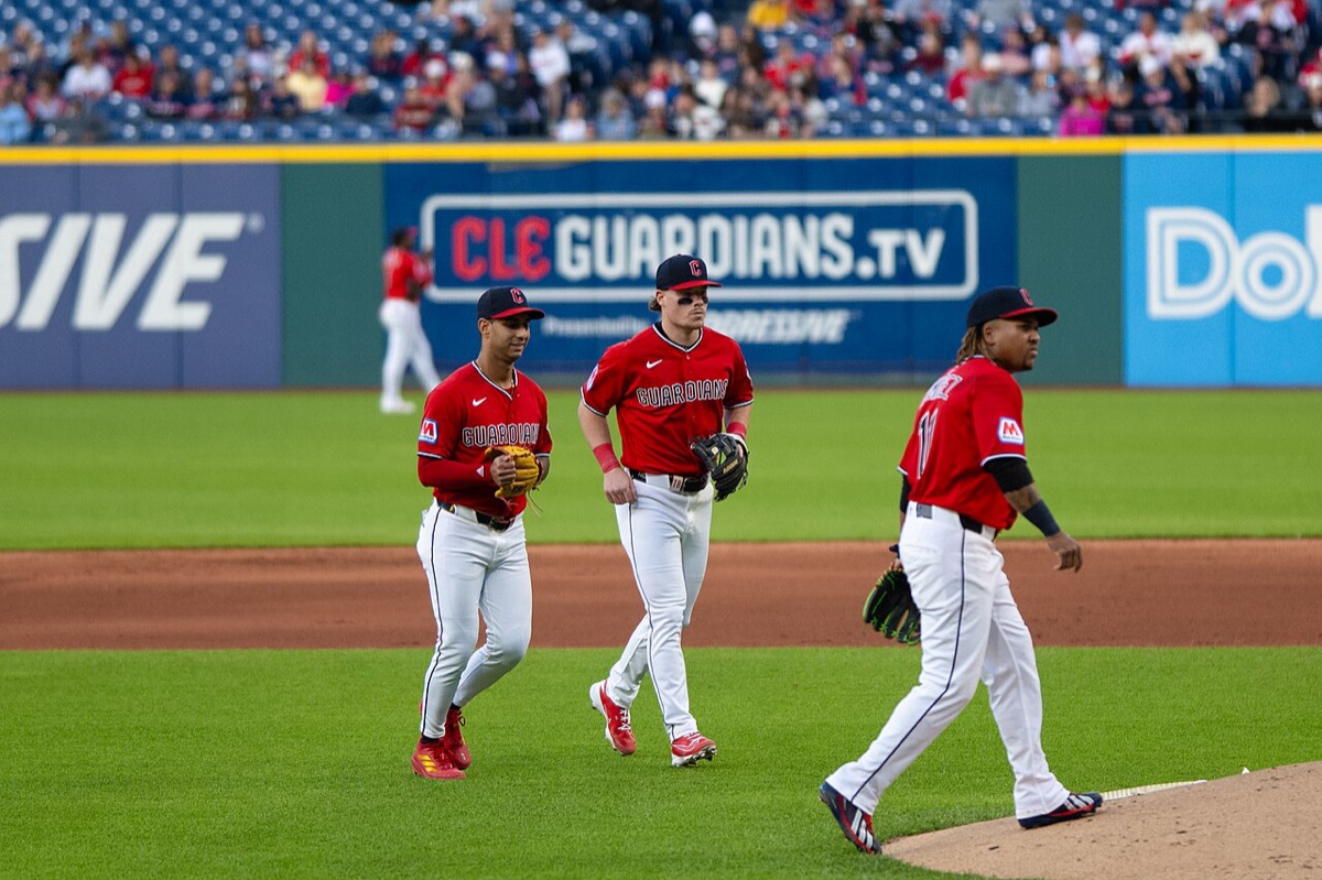 Foto de archivo: tres jugadores de los Cleveland Guardians con camiseta roja, entre ellos José Ramírez con el número 11, caminan por el cuadro de Progressive Field, con un cartel azul de CLE Guardians.tv y las tribunas detrás