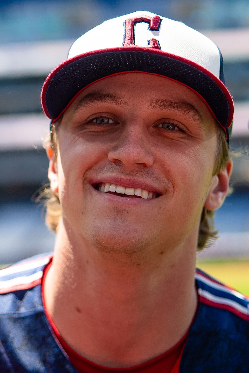 Foto de archivo: Petey Halpin, de los Cleveland Guardians, sonriendo, con gorra blanca y azul con la C roja y camiseta azul con vivos rojos, en un estadio desenfocado detrás