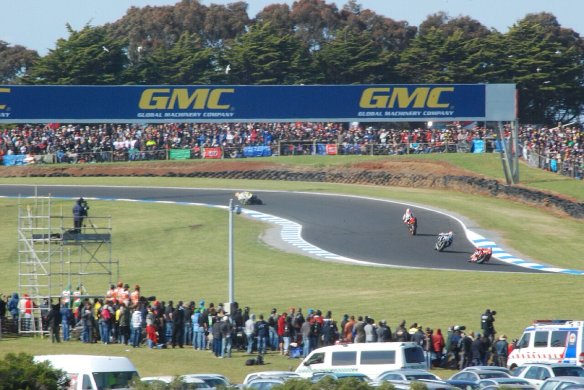 Foto de archivo: tres motos encaran una curva de Phillip Island delante de una tribuna llena de público, con la pista rodeada de pasto