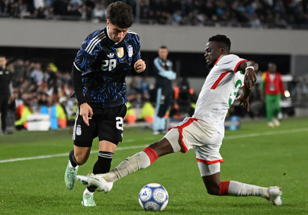 Un jugador de la Selección Argentina con la camiseta 28 conduce la pelota ante la barrida de un defensor de Burkina Faso