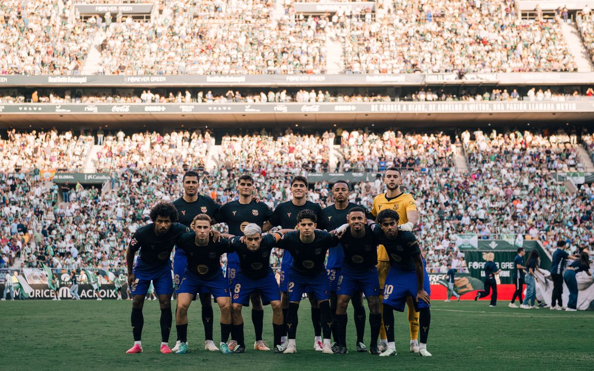 Los once titulares del Barcelona, con la camiseta azul oscura y pantalón azul, posan para la foto de equipo antes del partido en La Cartuja, con la tribuna llena detrás (foto: prensa FC Barcelona)