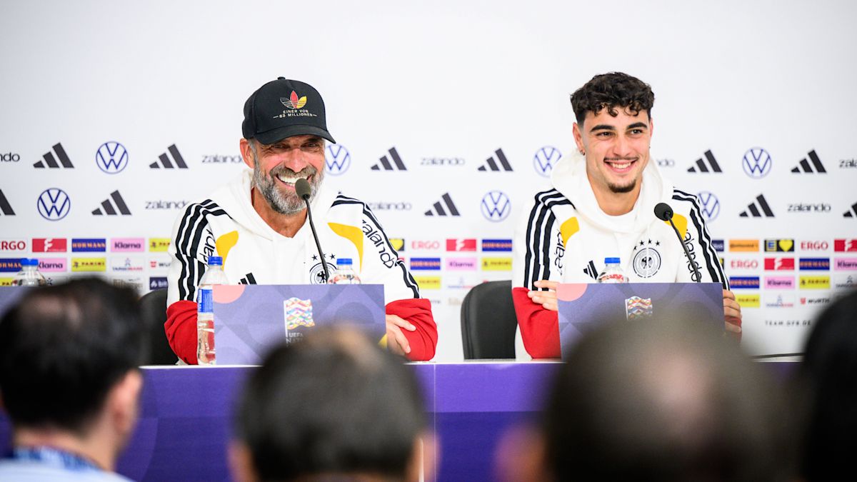 Jürgen Klopp, con gorra negra, y Aleksandar Pavlović sonríen en la conferencia de prensa de la selección alemana, frente a un panel de patrocinadores