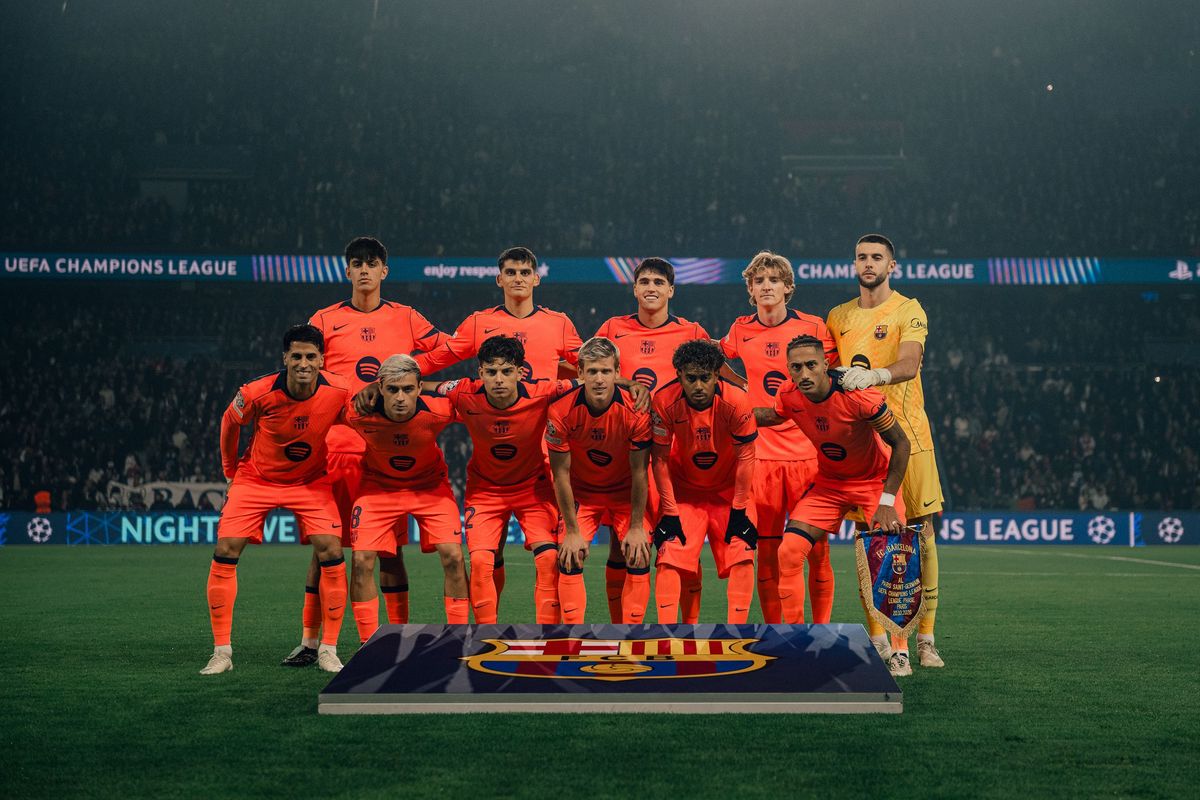 El equipo titular del Barcelona, con la camiseta naranja, posa para la foto antes del partido en el Parque de los Príncipes, con las tribunas iluminadas detrás (foto: FC Barcelona)