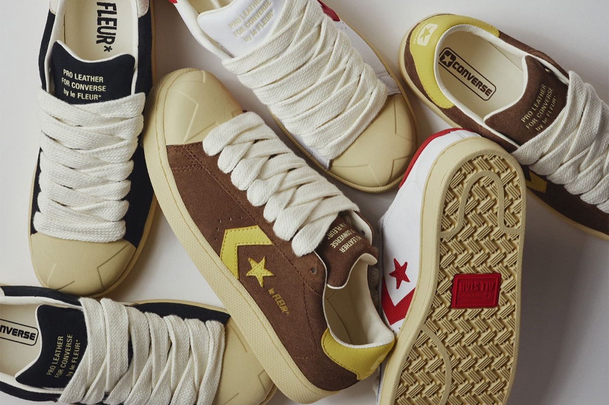 Varios pares de la Converse Pro Leather de GOLF le FLEUR* apilados sobre fondo blanco: uno de gamuza marrón con la estrella y el chevron amarillos, uno blanco con detalles rojos, uno negro, todos con cordones gruesos color crudo, puntera de goma y la leyenda Pro Leather for Converse by le FLEUR* en la lengüeta