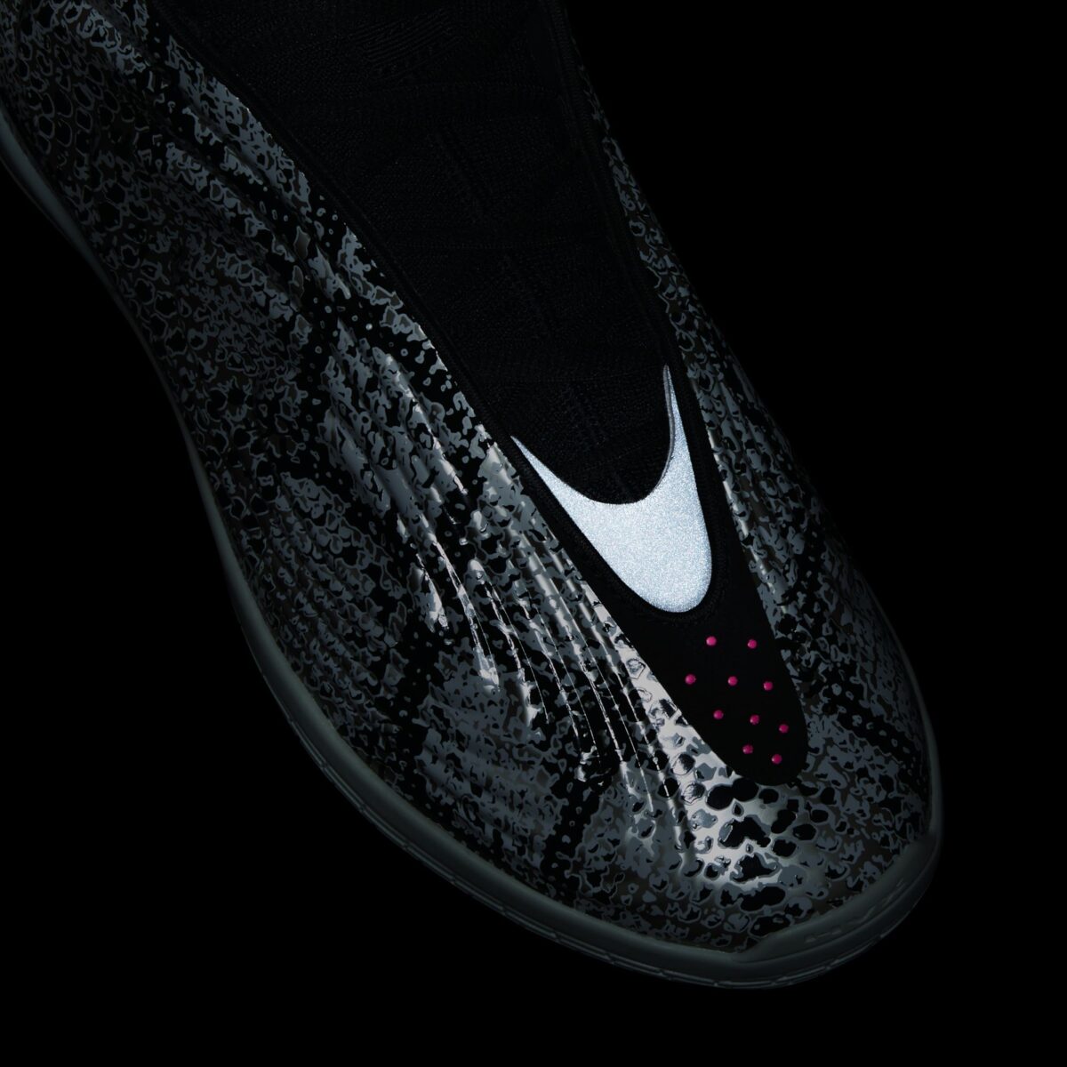 Primer plano de la punta de la adidas Harden Vol. 10 Snakeskin sobre fondo negro, con la pieza reflectiva del centro brillando en blanco, el estampado de víbora oscurecido y una hilera de puntos rosas