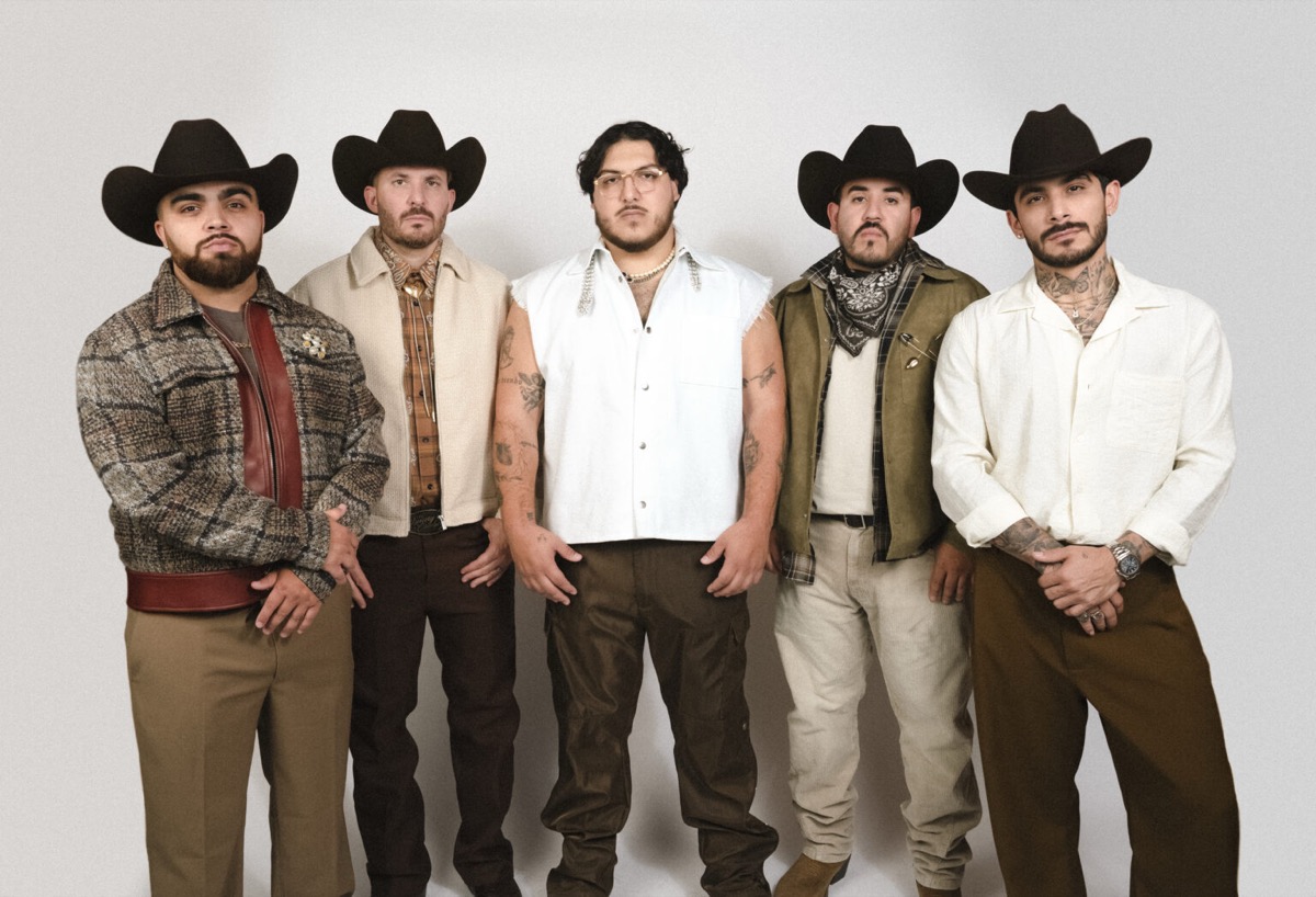 Foto de prensa de Grupo Frontera: los cinco integrantes de pie frente a un fondo blanco, cuatro con sombrero texano negro y el del centro con anteojos y chaleco blanco sin mangas