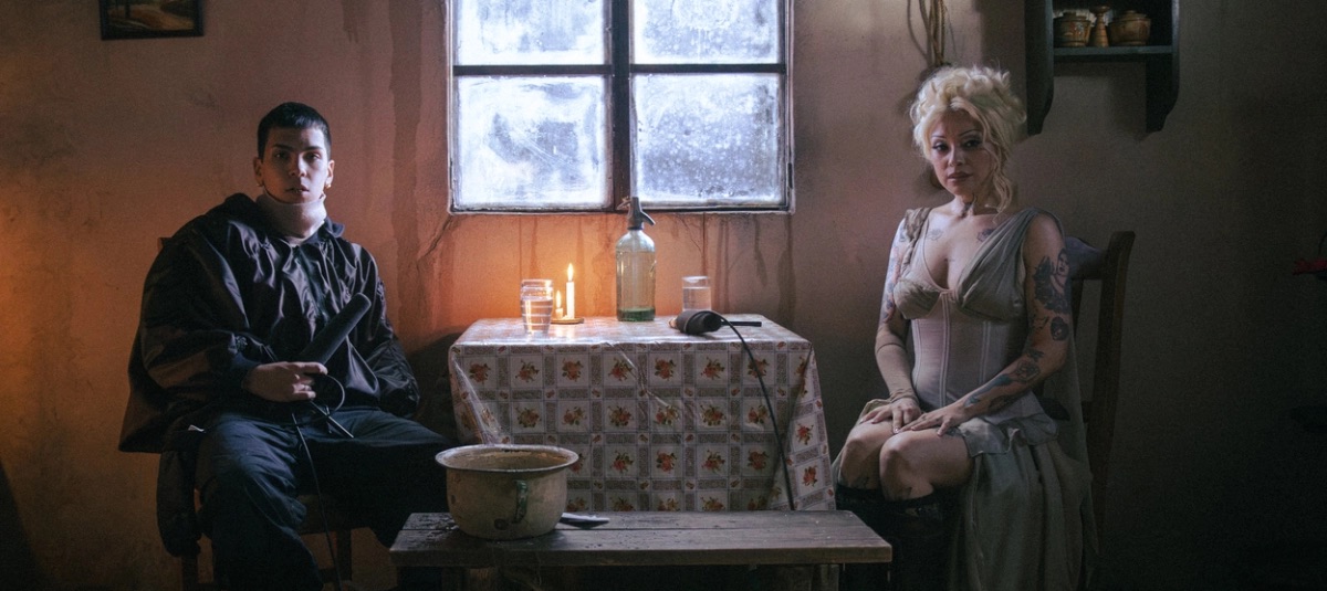 Milo J y Mon Laferte sentados en una casita a la luz de una vela, en una imagen de prensa de La Jangada