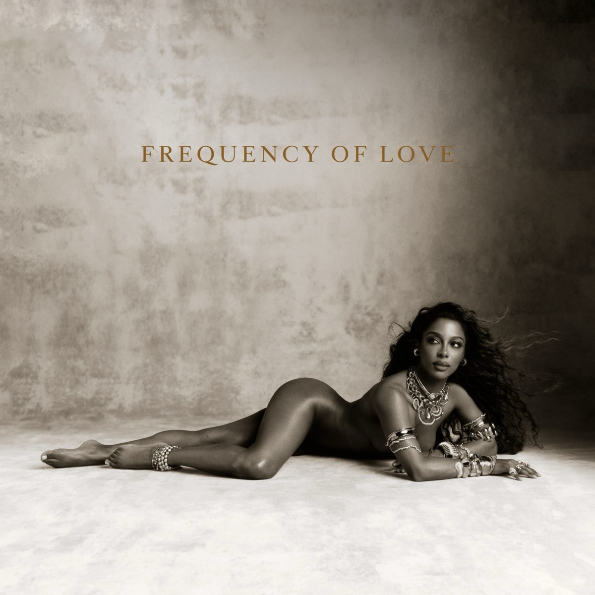 Portada oficial de Frequency of Love de Victoria Monét: la artista recostada sobre un piso claro, con joyas doradas y el título en letras ocres sobre un fondo sepia
