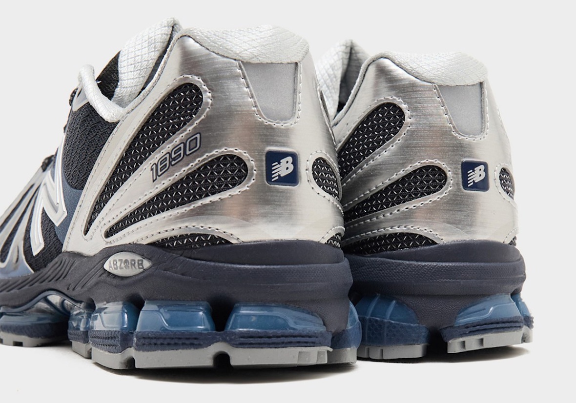 Vista trasera del par de New Balance 1890 Metallic Blue, con el talón plateado de textura cepillada, el número 1890, el logo de New Balance en un parche azul, la placa ABZORB y las cápsulas azules translúcidas sobre la suela gris
