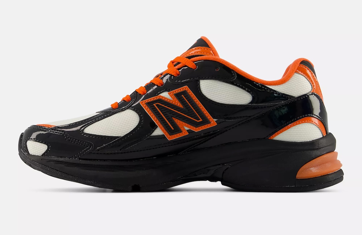 Vista lateral interna del New Balance 2010 Halloween sobre fondo gris claro, con el charol negro brillante, los paneles de malla crema, la N con borde naranja, el cuello naranja y un pod naranja en el talón