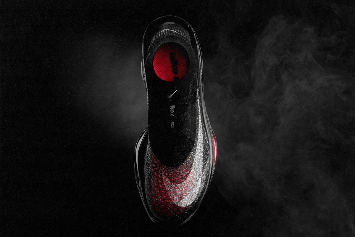 Vista desde arriba de la Nike Apex negra sobre fondo oscuro, con el Flyknit en degradé de gris a rojo, el Swoosh blanco y el interior rojo sin plantilla