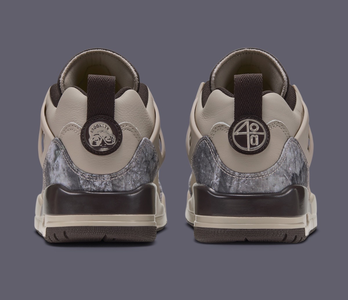 Vista trasera del par del Jordan Spizike Low Realtree Camo, con tiradores marrón oscuro, una insignia circular con la palabra Brooklyn en un talón y otra con el número 40 en el otro, sobre el camuflaje gris del contrafuerte
