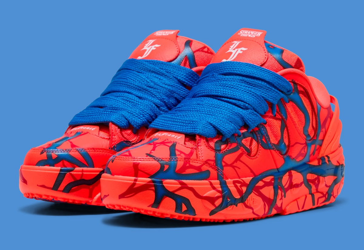 Par de PUMA LaFrancé Stranger Things sobre fondo azul, con upper y suela rojo intenso cubiertos de ramas azules y rojo oscuro, cordones azules extra anchos y el logo de Stranger Things con las iniciales LF en la lengüeta