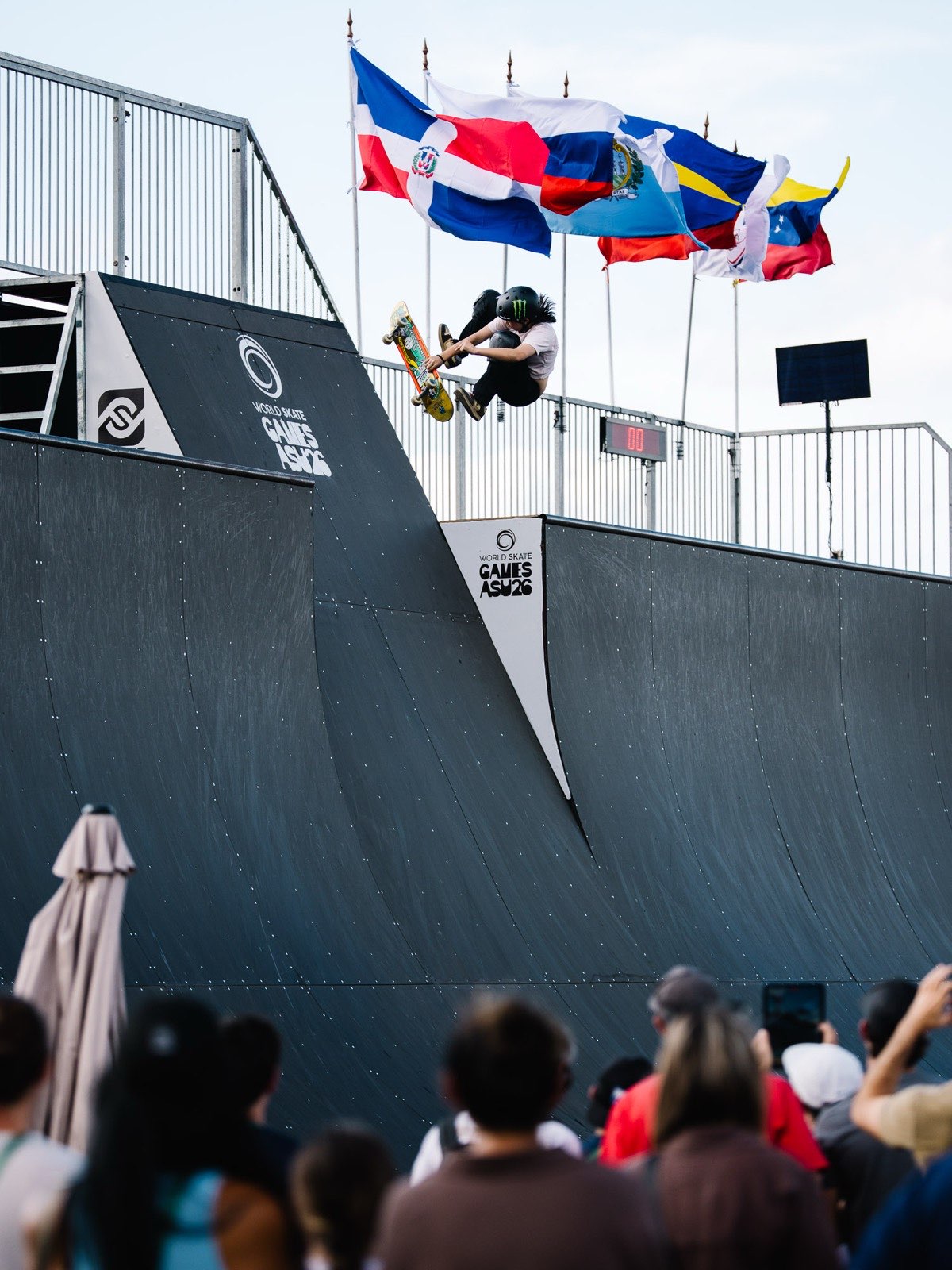Mizuho Hasegawa hace un aéreo sobre la rampa de vert de los World Skate Games ASU26, con banderas y público abajo