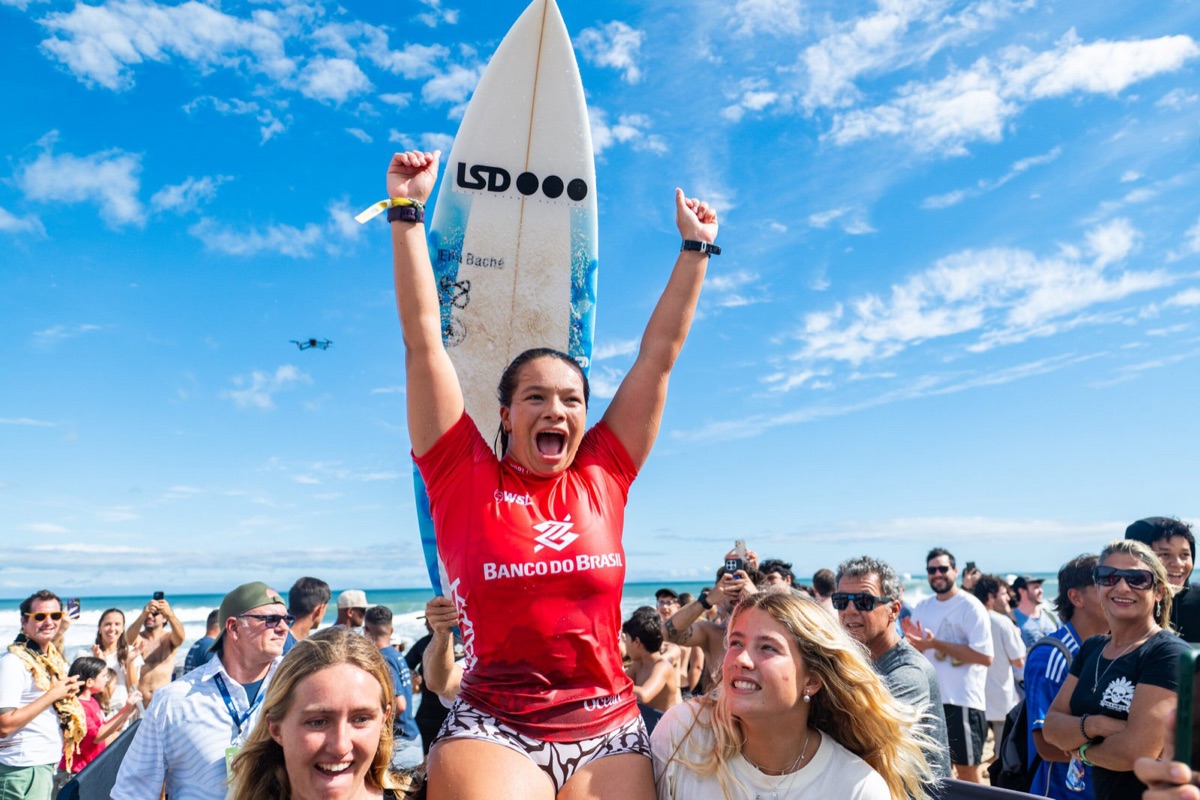 Charli Hately grita con los brazos en alto, en andas, con su tabla detrás y la playa de Maresias llena de gente