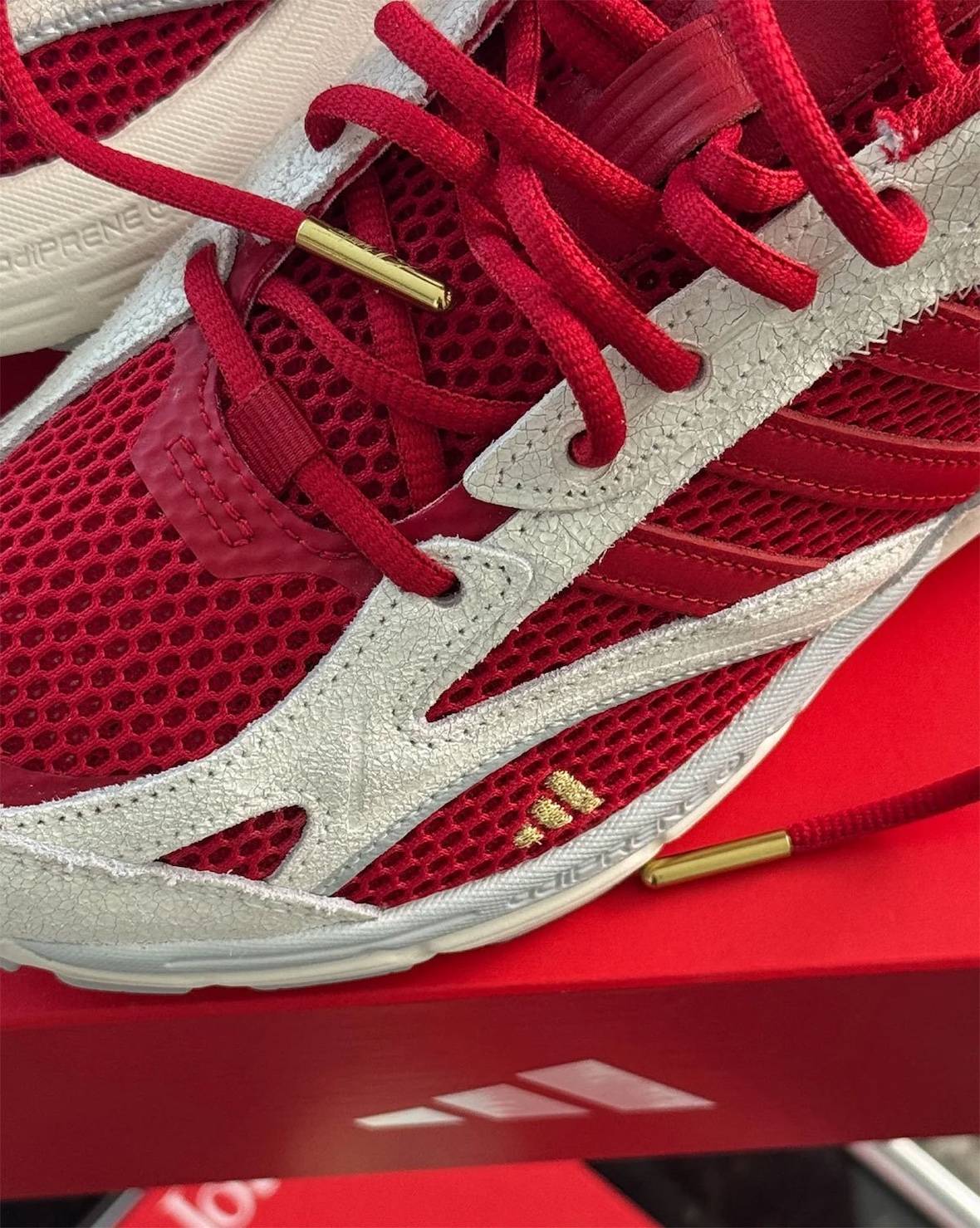 Detalle del Tyrrell Winston x adidas Spiritain 2000 con la malla roja, las capas crema con textura gastada, el logo de tres barras en dorado y una punta de cordón dorada